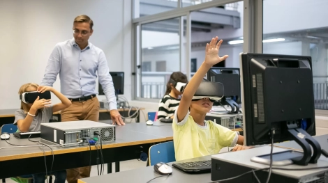 Group of multiethnic kids wearing VR headsets and teacher watching them. Adorable mixed-raced children learning virtual reality and sitting at computer lesson. Informatics and education concept